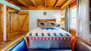Un dormitorio de cabaña de madera con una cama, una decoración de cabeza de oso y una ventana con cortinas.
