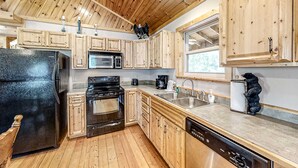 A kitchen with wooden cabinets, a black refrigerator, a microwave, an oven, a sink, and a dishwasher. - Secluded Retreat, Sleeps 4・Furnished Deck・Hot Tub (Sevierville)
