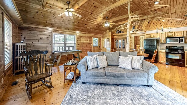 A wooden cabin interior with a living room featuring a sofa, rocking chair, and a dining area with a table and chairs. The kitchen area includes appliances and cabinets. - Secluded Retreat, Sleeps 4・Furnished Deck・Hot Tub (Sevierville)