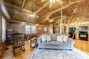 A wooden cabin interior with a living room featuring a sofa, rocking chair, and a dining area with a table and chairs. The kitchen area includes appliances and cabinets. - Secluded Retreat, Sleeps 4・Furnished Deck・Hot Tub (Sevierville)