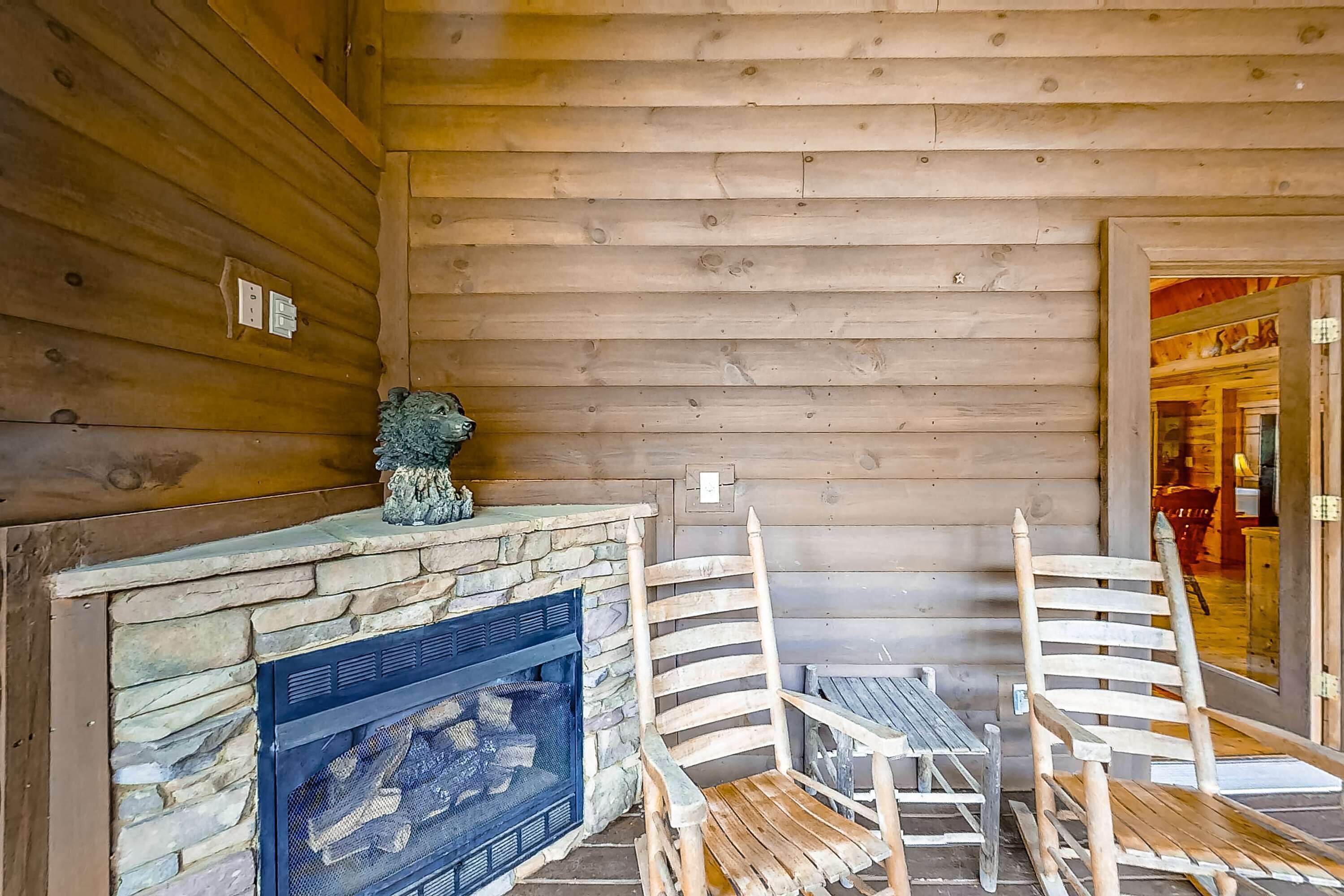 L’intérieur d’un chalet en bois, avec une cheminée en pierre, deux chaises en bois et une petite statue.