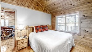 A wooden cabin bedroom with a bed, nightstand, lamp, and a window with blinds. - Secluded Retreat, Sleeps 4・Furnished Deck・Hot Tub (Sevierville)