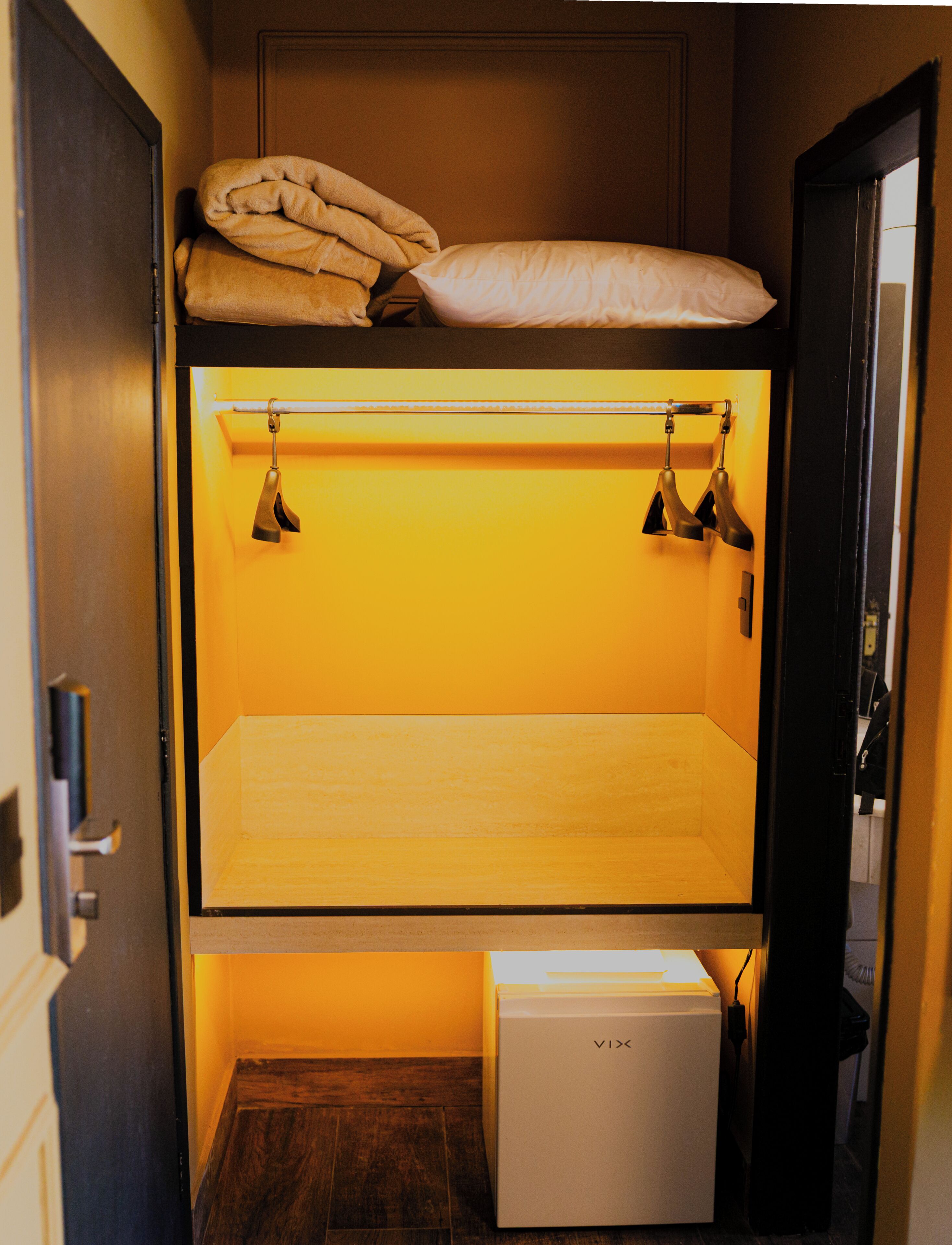 A bunk bed with a mattress and pillows on top, a small bedside table, and a box on the floor.