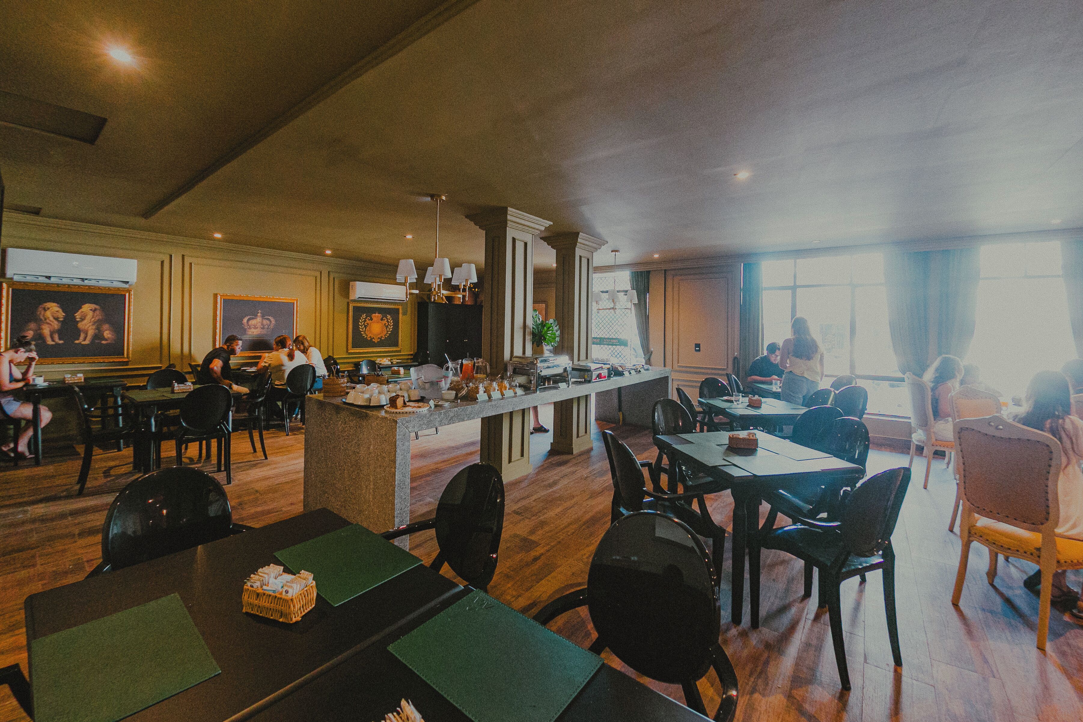 Un restaurante con mesas y sillas de madera, una zona de bar y cuadros en las paredes.