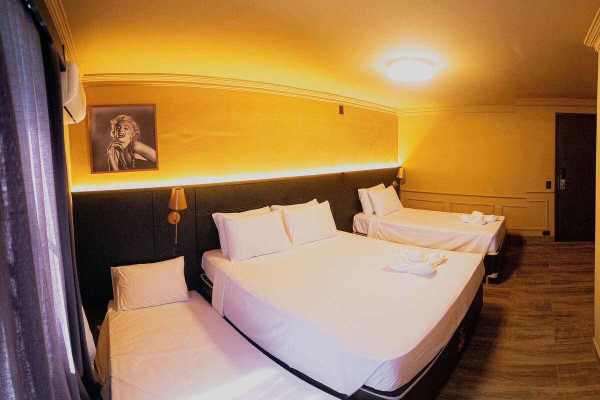 A hotel room with two beds, a nightstand with a lamp, a framed picture on the wall, and a door.