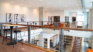 A modern interior with a mezzanine level, wooden flooring, and a glass railing overlooking a lower level with seating and tables. - Landing | Amazing Studio, Pool, Yoga Studio (Birmingham)