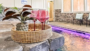 Un banc en pierre avec un panier tressé et une plante en pot, une piscine éclairée de lumières violettes et un panneau indiquant qu’il est interdit de plonger.