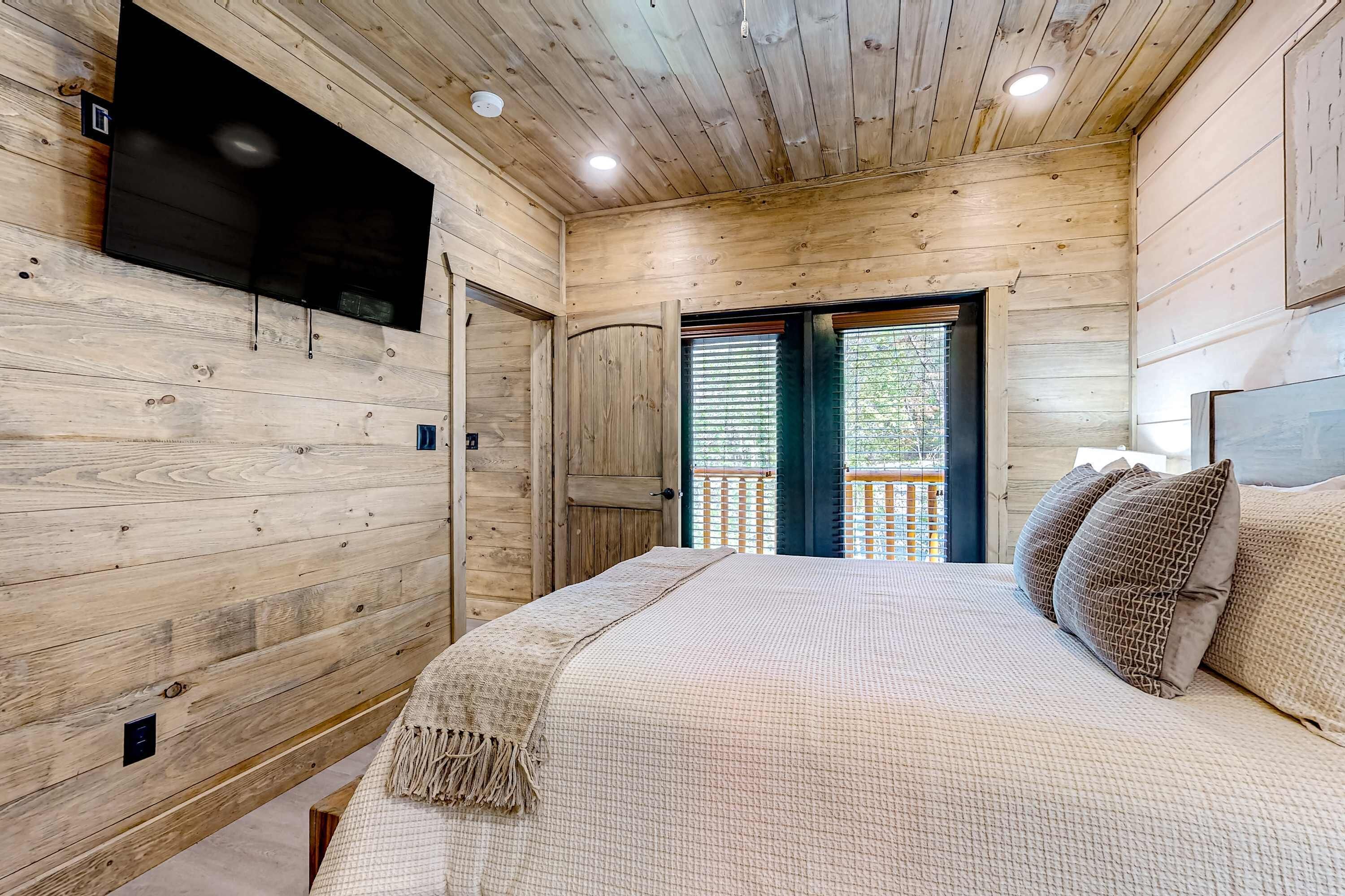 A wooden-paneled room with a bed, a TV mounted on the wall, and a balcony with a view.
