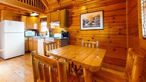 A wooden cabin interior with a kitchen area, wooden dining table, and chairs. - Adorable log cabin with front-back deck and hot tub (Pigeon Forge)