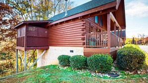 A log cabin with a balcony and a small wooden structure on stilts. - Adorable log cabin with front-back deck and hot tub (Pigeon Forge)