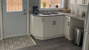 A compact kitchen with white cabinets, a stainless steel sink, and a window with potted plants. - Belmont Stayover (Belmont)