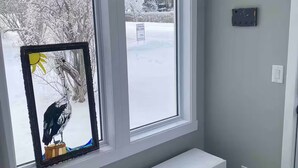 A room with a bench by a window, a wall clock, and a view of a snowy landscape. - Belmont Stayover (Belmont)