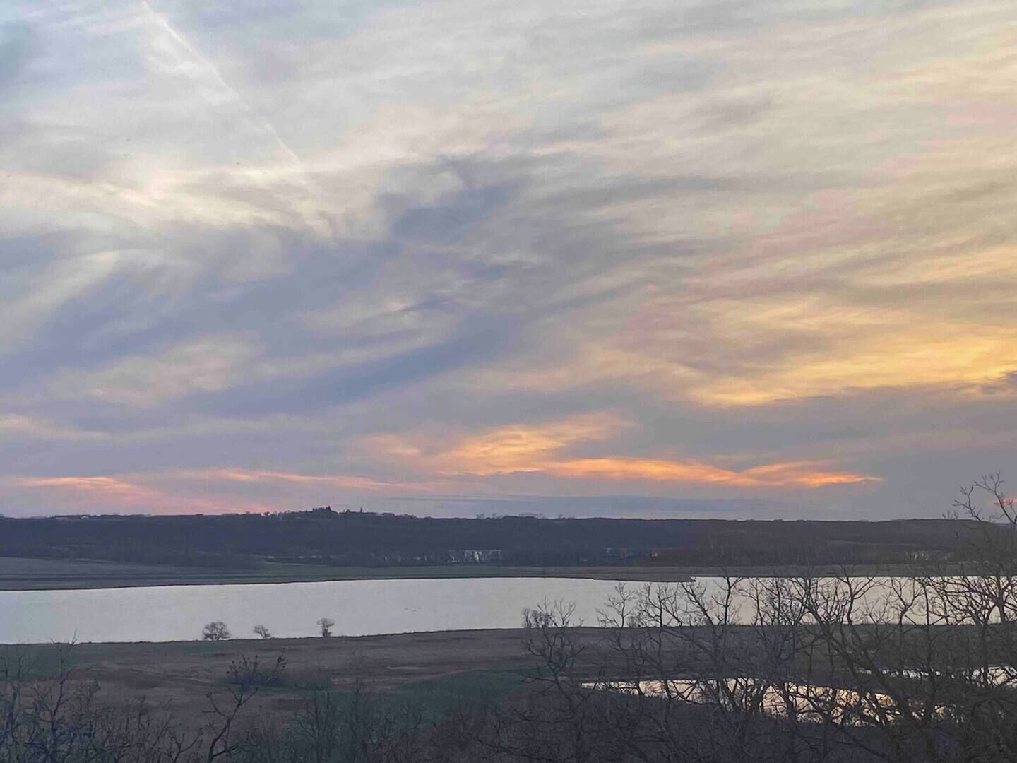 Un paysage comprenant une étendue d’eau, des arbres et un ciel nuageux.