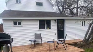 A white house with a wooden deck, a grill, and two chairs. - Belmont Stayover (Belmont)