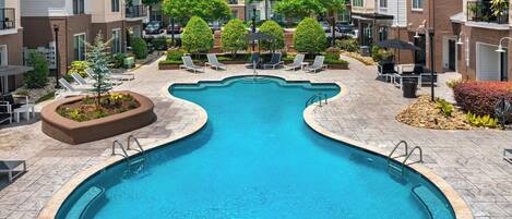 A swimming pool with a wavy design, surrounded by lounge chairs and potted plants.