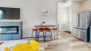 Eine moderne Küche mit einem Edelstahl-Kühlschrank, einem Holztisch mit Barhocker und einem wandmontierten Flachbildfernseher.