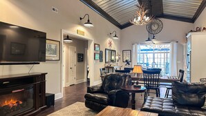 A living room with a fireplace, leather sofas, a dining area with a chandelier, and a kitchen in the background. - Waterfront Cabin Retreat・Dock・Firepit・Grill・Games (Sharps Chapel)