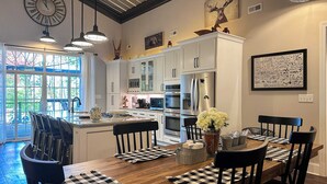 A modern kitchen with white cabinets, stainless steel appliances, and a wooden dining table with checkered placemats. - Waterfront Cabin Retreat・Dock・Firepit・Grill・Games (Sharps Chapel)