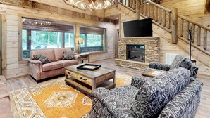 A cozy log cabin interior with a fireplace, a sofa, a coffee table, and a staircase. - Elegant Lodge, for 12・Pool・Hot Tub・Theater・Games (Sevierville)