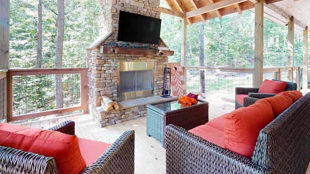 A covered outdoor seating area with wicker furniture, a stone fireplace, and a TV mounted on the wall. - Elegant Lodge, for 12・Pool・Hot Tub・Theater・Games (Sevierville)