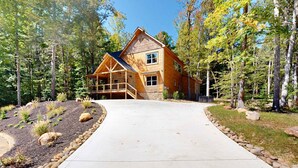 A large log cabin with a stone foundation, a wooden deck, and a driveway leading to the entrance. - Elegant Lodge, for 12・Pool・Hot Tub・Theater・Games (Sevierville)