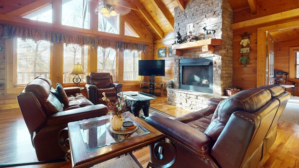 A cozy living room with wooden beams, a stone fireplace, leather sofas, and a flat-screen TV. - Mtn View Cabin, Sleeps 12・Game Room・Hot Tub・Pool (Sevierville)