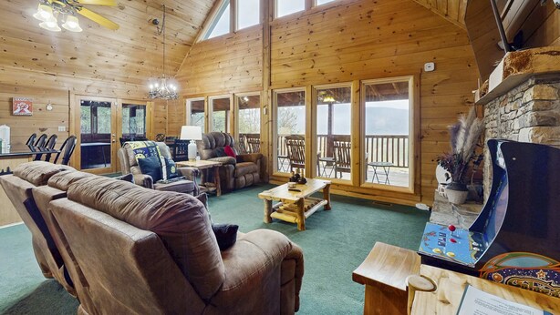 Une vaste cabane en bois dotée d’un grand espace de vie, de nombreux coins salon, d’une cheminée et de grandes fenêtres offrant une vue sur l’extérieur.