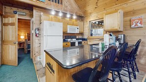 Une cuisine rustique aménagée dans une cabane en bois, avec un îlot central, des placards en bois, un four à micro-ondes et un réfrigérateur.