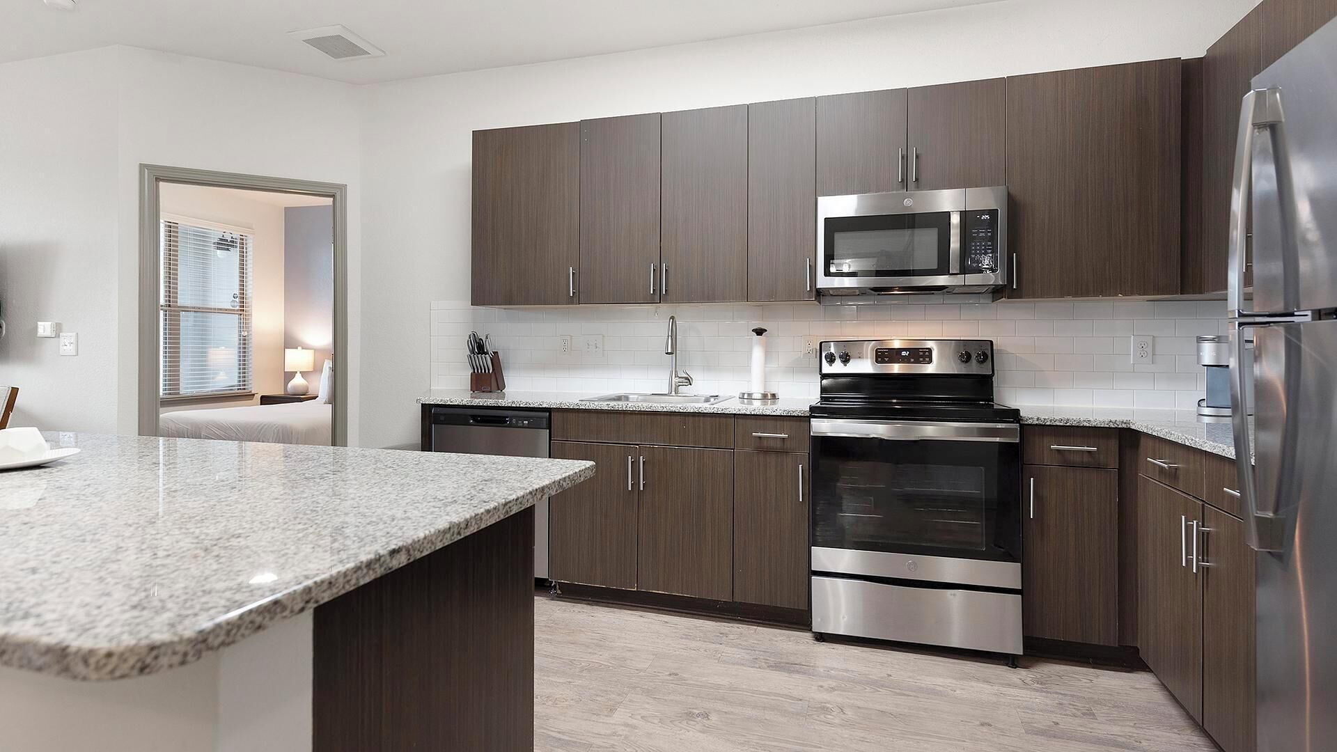 A modern kitchen with dark wood cabinets, stainless steel appliances, and a granite countertop.
