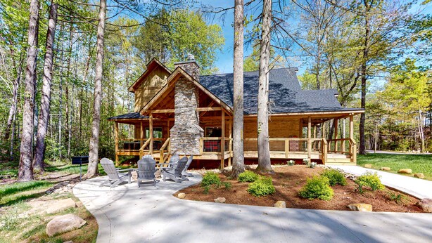Une cabane en rondins avec une cheminée en pierre, une terrasse en bois et un espace salon extérieur.