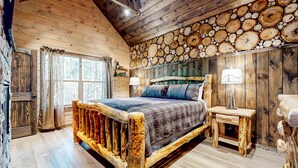 Une chambre rustique en bois, avec un lit, une table de chevet et un mur décoré de motifs représentant des cernes d'arbres.