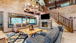 L'intérieur de cette vaste cabane en rondins est agrémenté d'un grand escalier en bois, d'une cheminée en pierre et d'un coin salon confortable avec des coussins à motifs.