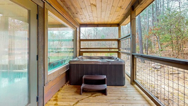 Eine Holzterrasse mit Whirlpool, einem kleinen Hocker und einer Glastür zu einem Raum.