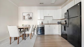 Eine moderne Küche mit weißen Schränken, einem schwarzen Kühlschrank und einem Essbereich mit Tisch und Stühlen.