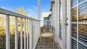 Eine Holzterrasse mit einem Stuhl, weißen Geländern und einem Gebäude mit großen Fenstern.