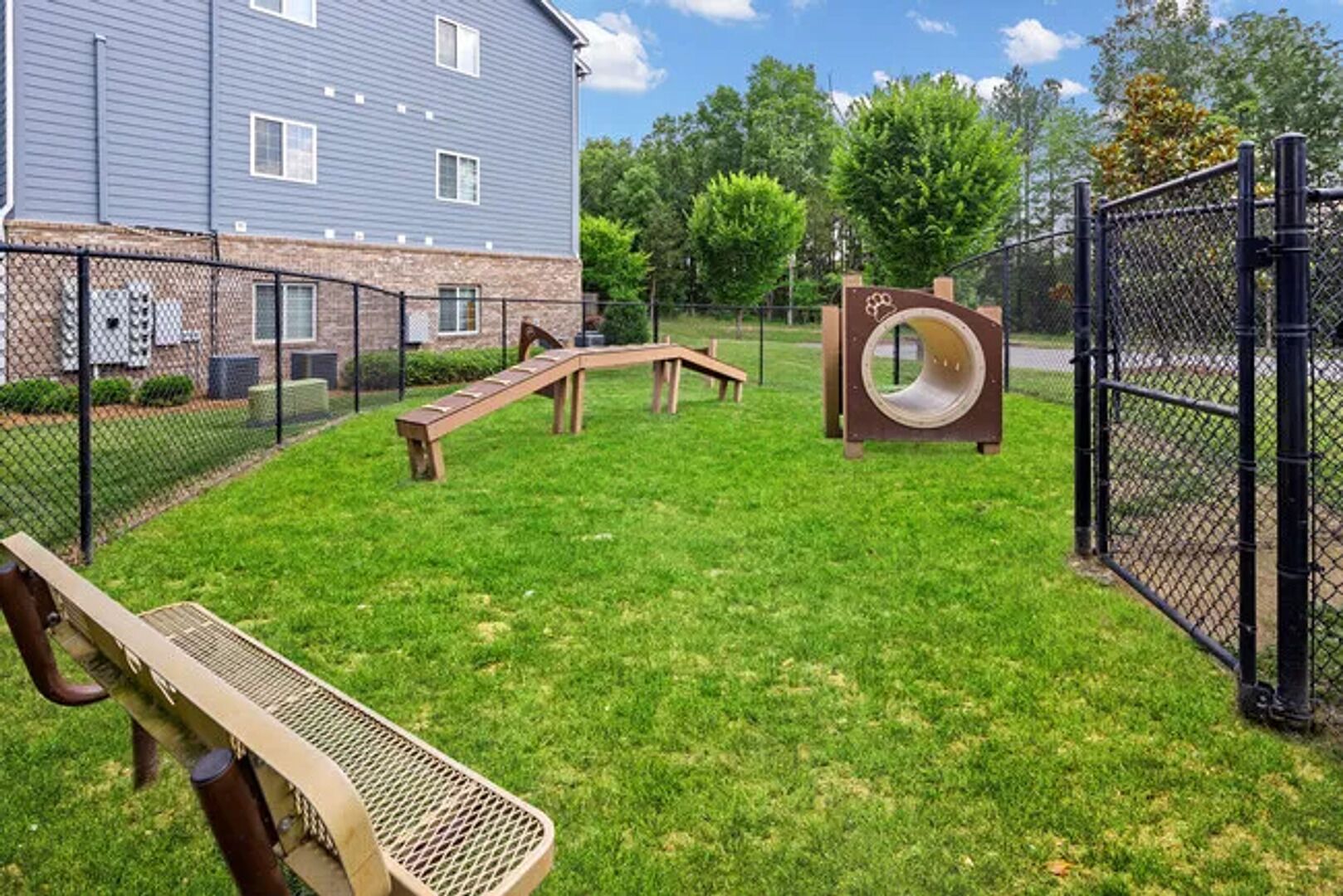 Un espace extérieur clôturé comprenant un banc en bois, un toboggan et une structure en forme de tunnel.