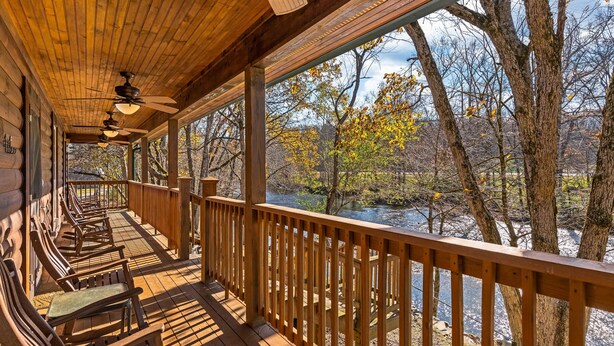Une terrasse en bois dotée d’une balustrade, qui offre une vue sur une rivière et est entourée d’arbres.