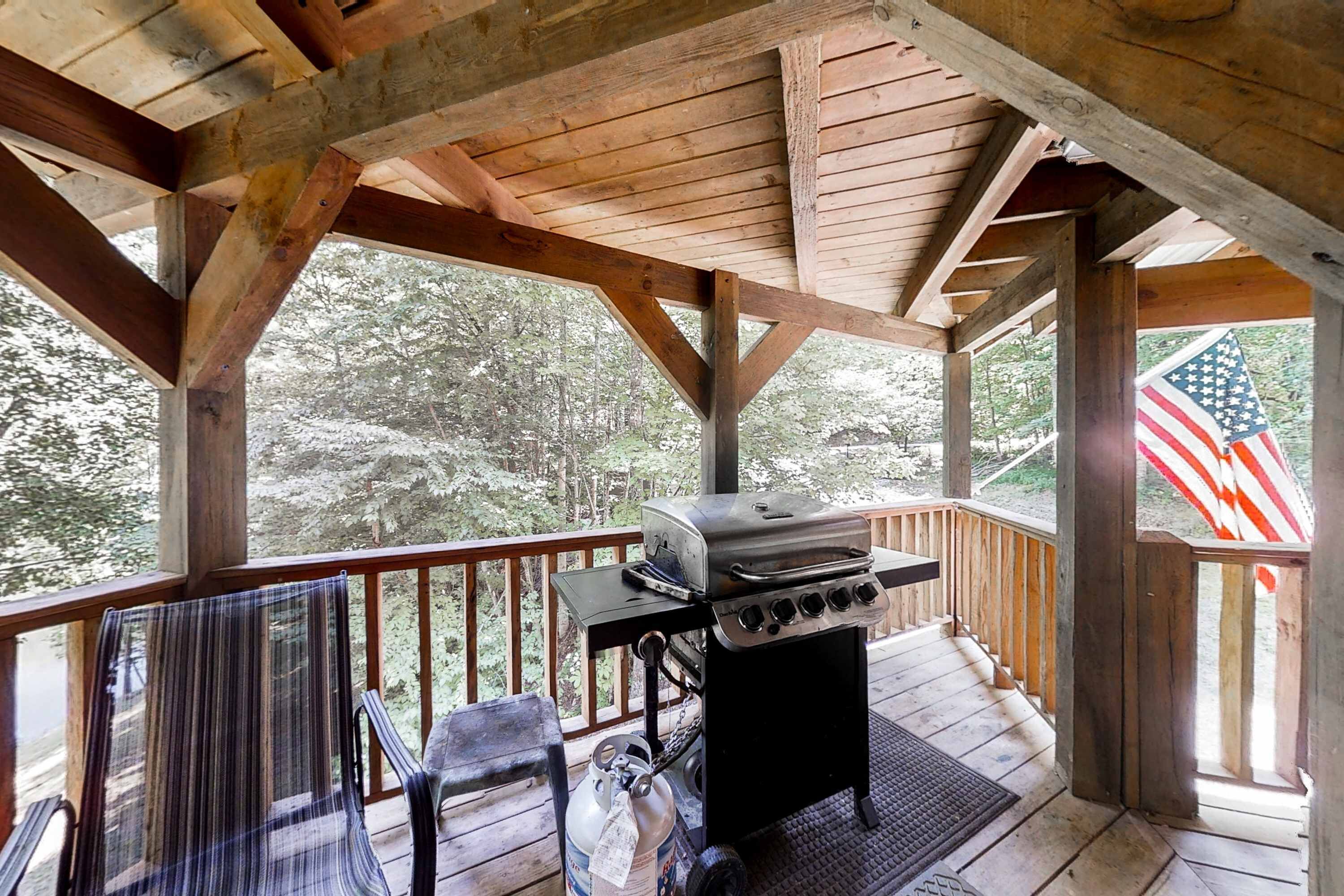 Un espacio al aire libre techado con una parrilla, sillas y vistas a árboles.