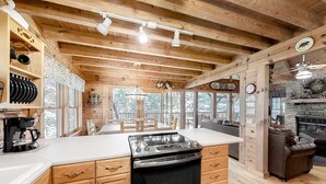 L’intérieur d’un chalet en bois comprend une cuisine équipée d’une cuisinière, d’un four et de plans de travail blancs.