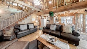 Un vaste espace de vie comprenant deux canapés en cuir, une table basse en bois et un escalier menant à un niveau supérieur.