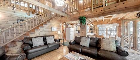 Un espacio habitable amplio con dos sofás de cuero, una mesa de centro de madera y una escalera que lleva a un nivel superior.