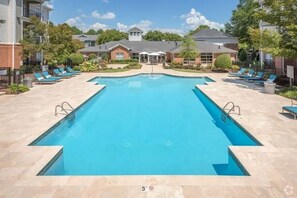 Ein rechteckiger Swimmingpool mit einer Tiefenmarkierung von 1,5 Metern, umgeben von Liegestühlen und einem Gebäude mit überdachter Terrasse im Hintergrund.