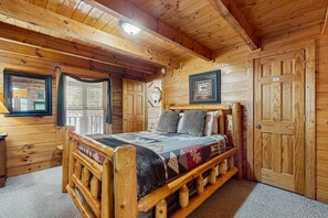 A wooden cabin room with a bed, wooden walls, a window, and a door. - Panoramic Mountain Views, Secluded Cabin, Hot Tub (Sevierville)