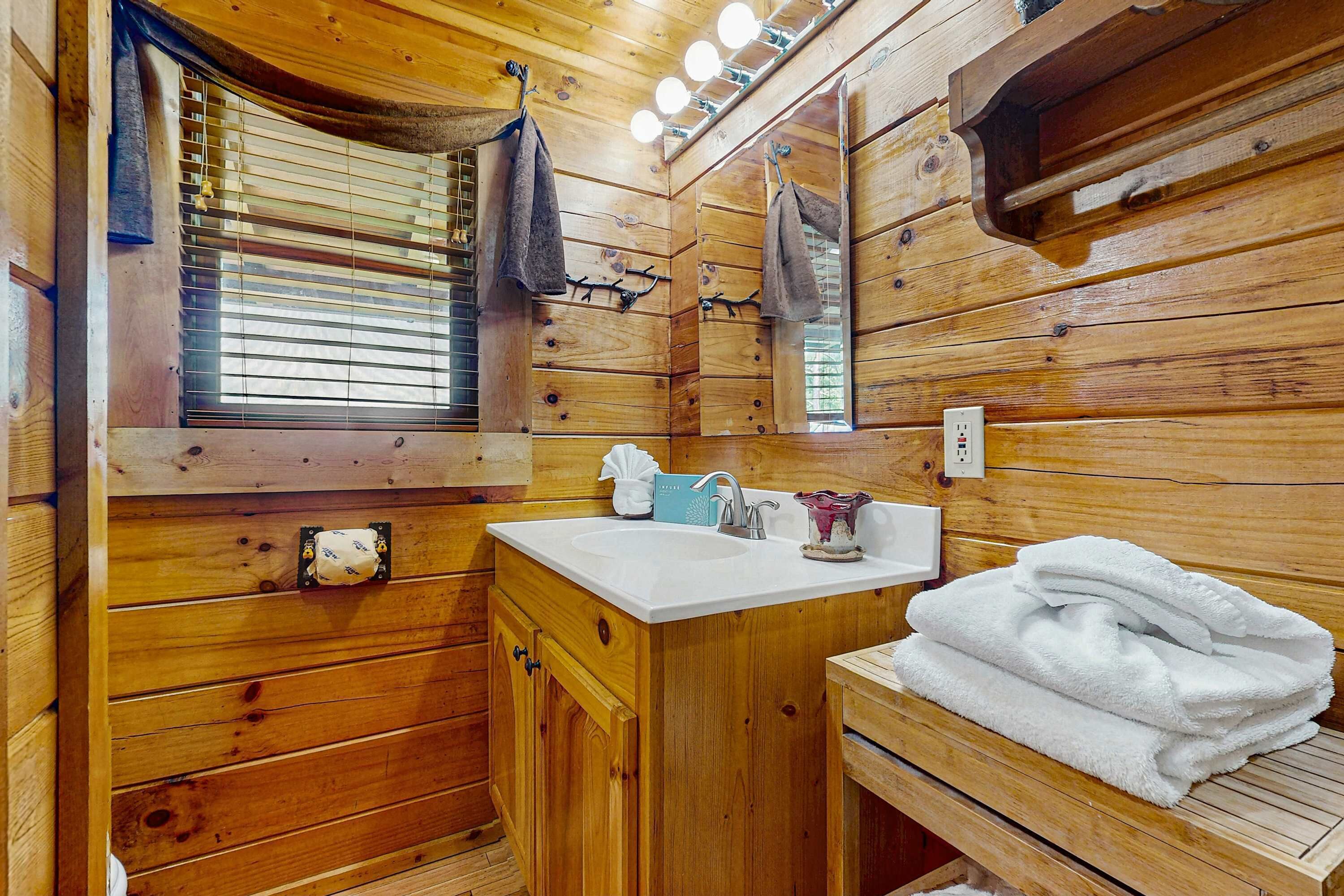 Un baño de cabaña de madera con lavamanos, espejo, toallero y ventana con persianas.