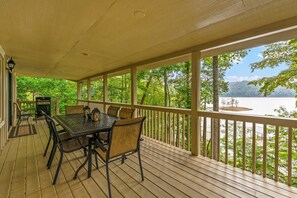 A covered outdoor deck with a table and chairs, overlooking a body of water and surrounded by trees. - Lakefront Norris Cabin Retreat・Dock・Games・Hot Tub (Sharps Chapel)