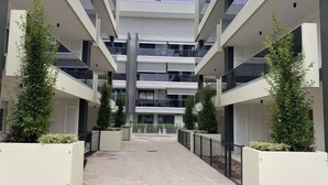 Un edificio moderno de varios pisos con un atrio central, balcones y jardineras con plantas.