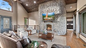 A spacious living room with a stone fireplace, leather sofas, and a large TV mounted on the wall. - Mtn View Home, Sleeps 8・Fireplace・Games・Hot Tub (Sevierville)