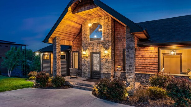 A stone and wood house with a sloped roof, a front porch with two chairs, and a well-lit entrance. - Mtn View Home, Sleeps 8・Fireplace・Games・Hot Tub (Sevierville)