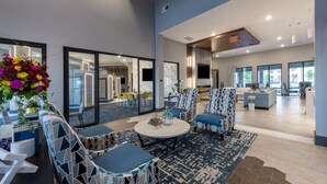 A modern hotel lobby with a round table, patterned chairs, a large floral arrangement, and a view of the dining area.