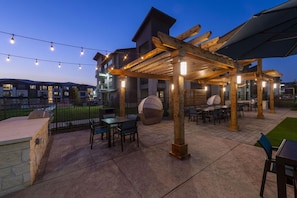 An outdoor patio area with a pergola, seating, and a barbecue grill.